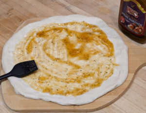 Spread the Spiedie marinade over the pizza dough.